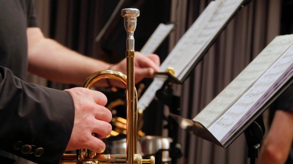 A player's hands on a trumpet beside a music stand.